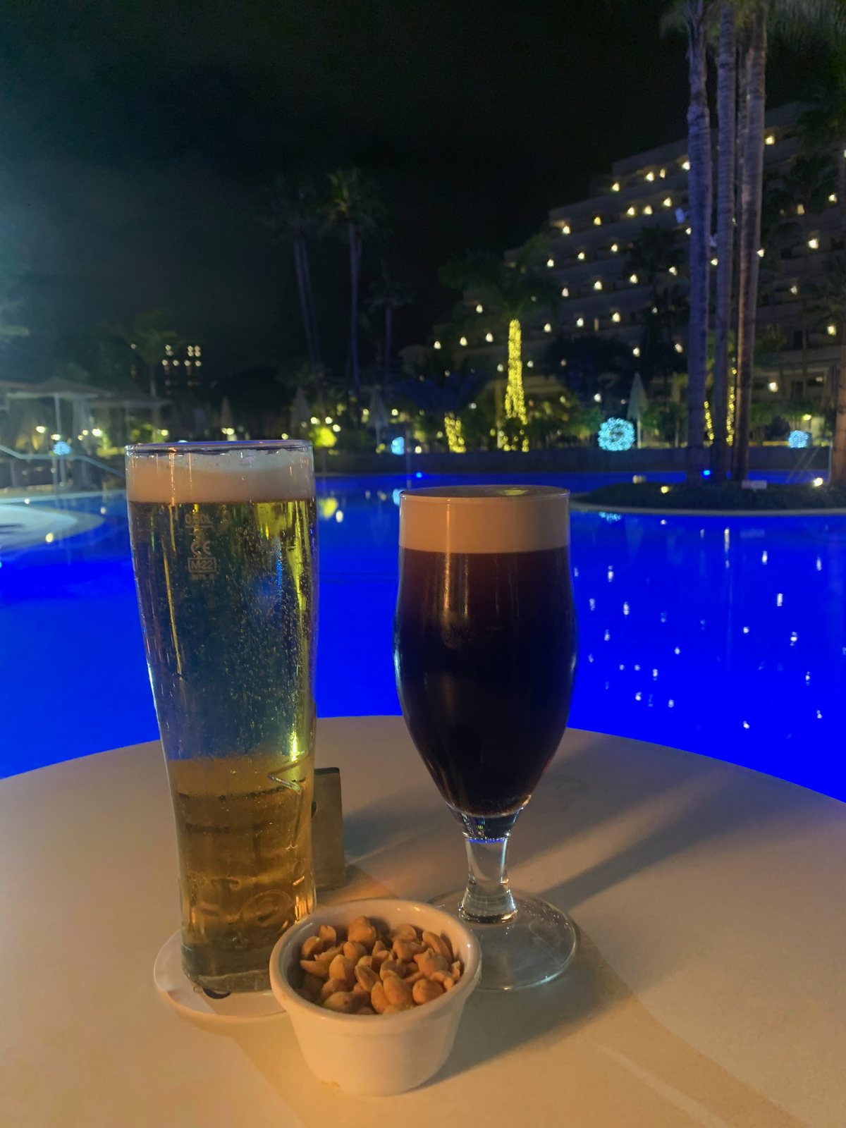 Two drinks and a bowl of snacks beside the illuminated pool at night